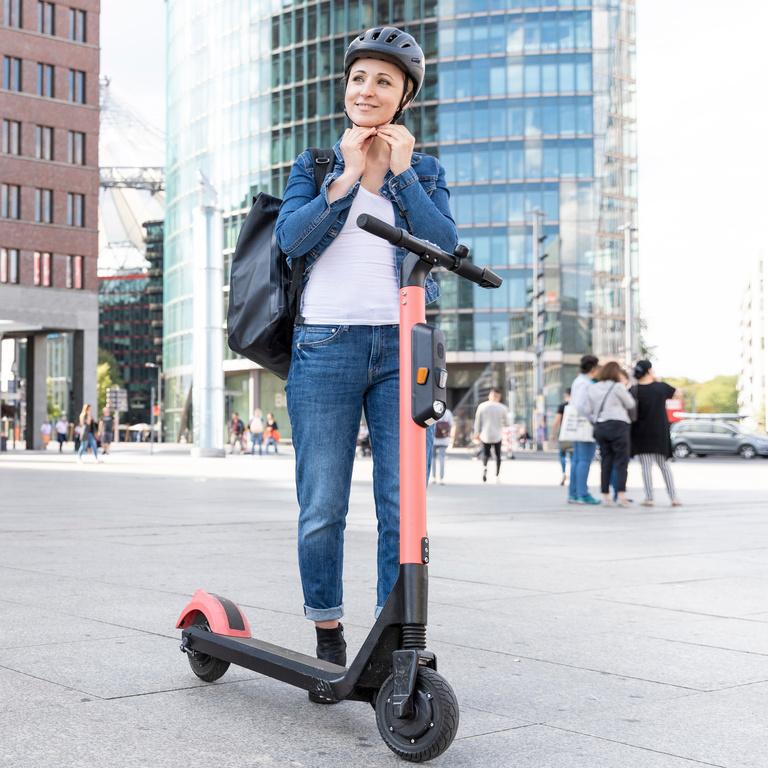 Woman with e-scooter in the city putting on helmet, Berlin, Germany
