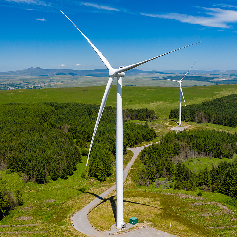 Aerial drone view of turbines at a large onshore windfarm on a green hillside