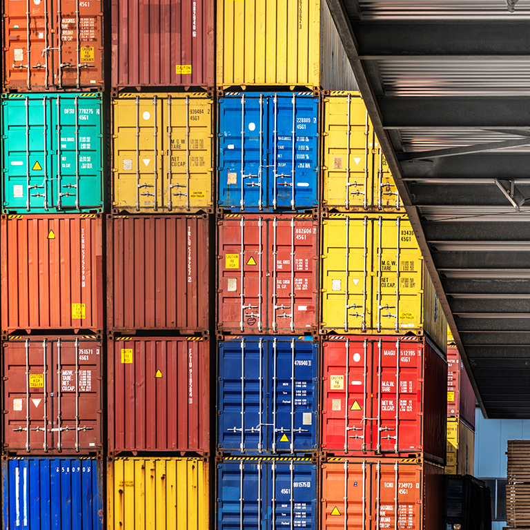 Rows of brightly colored shipping containers are neatly stacked in a warehouse. The vibrant hues create a striking visual effect against the industrial interior, showcasing their arrangement.