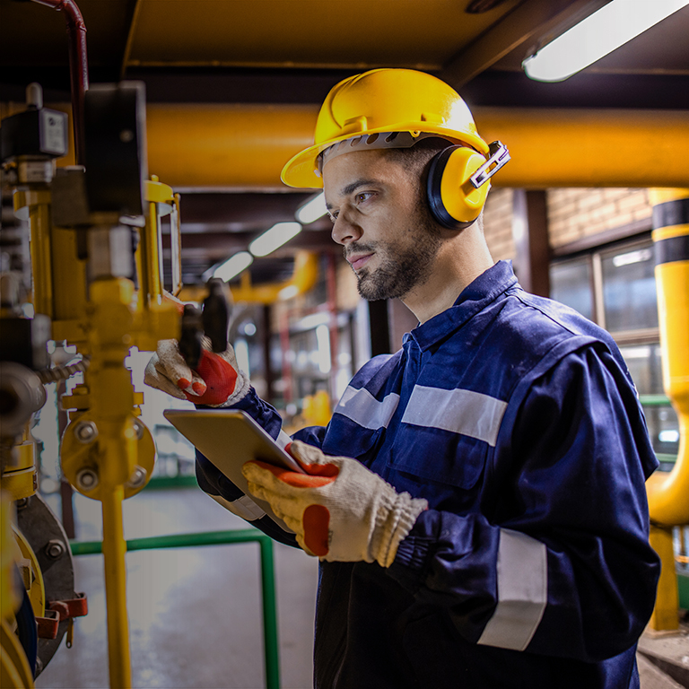 Heating plant technician standing by gas pipes and maintaining temperature inside power plant boiler room.