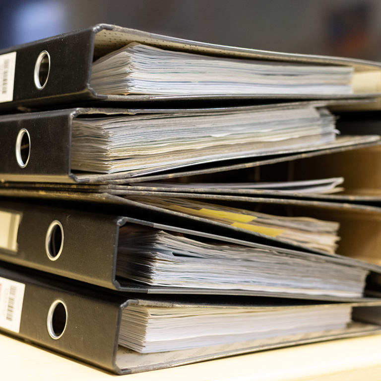 Files stacked on filing cabinet. A large pile of binders filled with papers