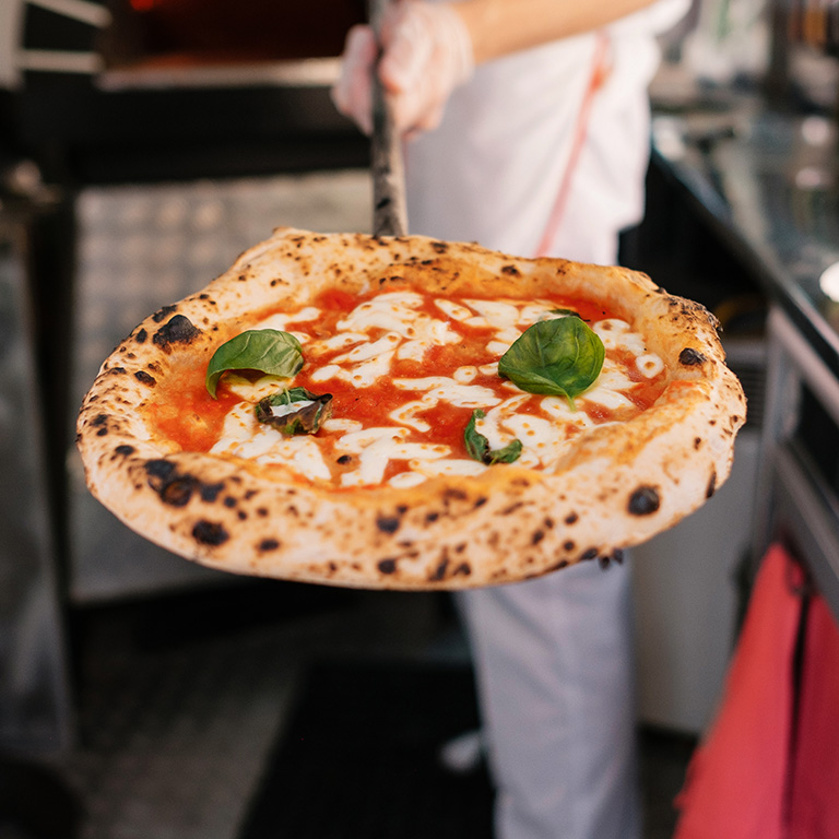 The process of making pizza. The cook shows the pizza that he got out of a wood-fired oven.