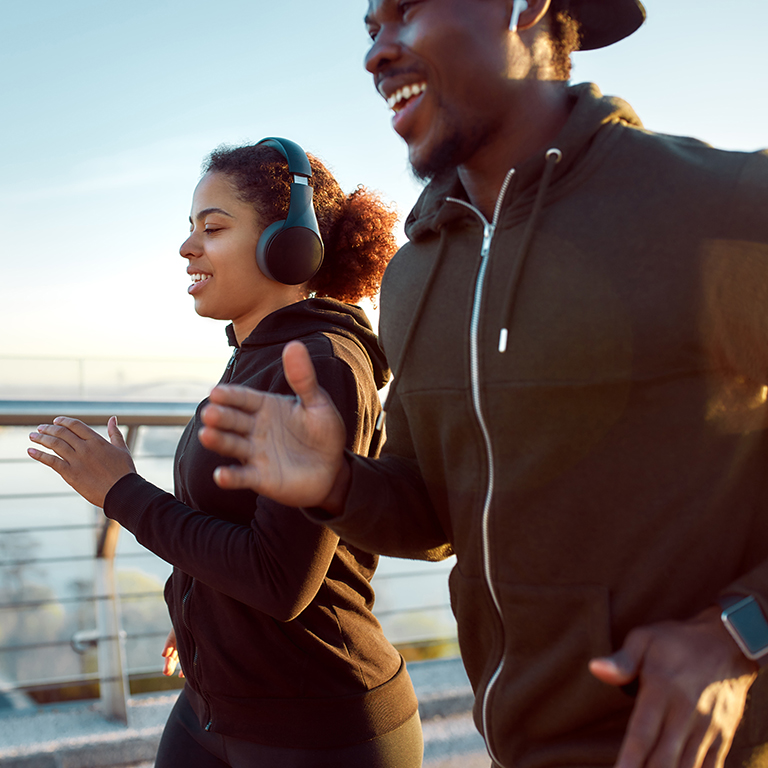 Young happy African couple in headphones jogging together on the bridge