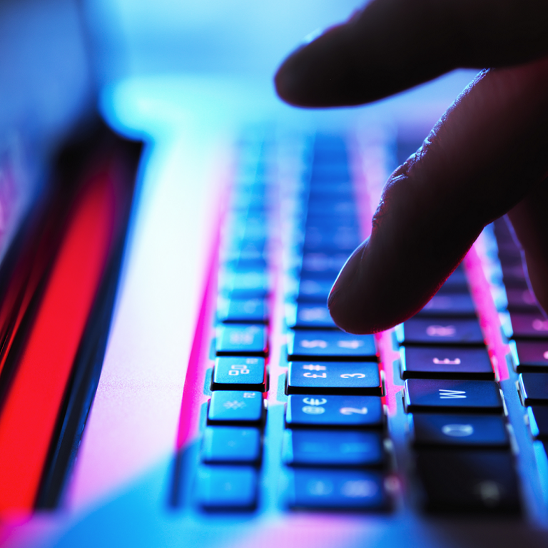 Close-up of fingers typing on a keyboard lit with blue and pink lights